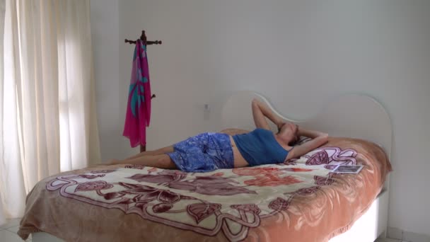 Жінка лежить на ліжку з планшетним ПК. Дівчина виходить з ліжка одягає хустку і залишає кімнату — стокове відео