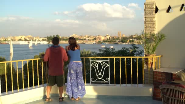 Жінка і чоловік стоять на терасі і дивляться на річку. Чоловік фотографує пейзаж — стокове відео