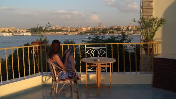 Mujer Sienta Una Terraza Con Vistas Río Utiliza Teléfono Inteligente — Vídeos de Stock