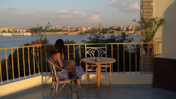 Mujer se sienta en una terraza con vistas al río y fuma — Vídeos de Stock