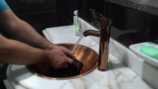 Мужчина в ванной стирает куртку в раковине — стоковое видео