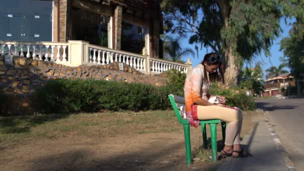 En kvinna sitter på en bänk i parken och smeker en kattunge i knäet — Stockvideo