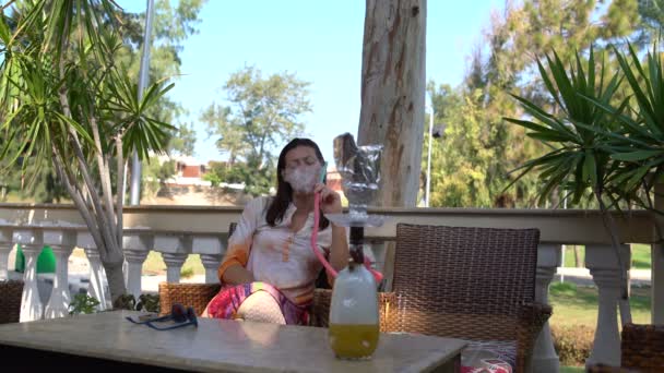Uma mulher senta-se a uma mesa e fuma shisha — Vídeo de Stock
