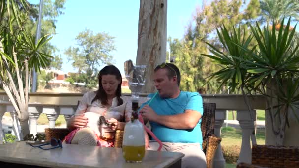 Un hombre fumando narguile en un café. Mujer jugando con un gatito — Vídeo de stock