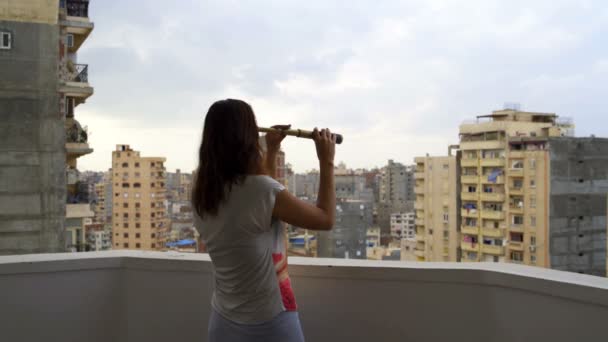 Mujer mira a la ciudad a través de un telescopio — Vídeos de Stock