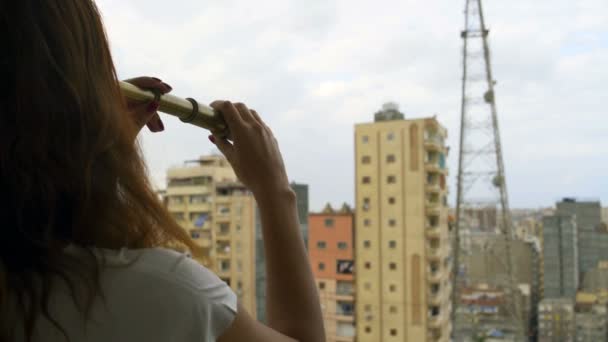 La mujer mira a la ciudad a través de un catalejo — Vídeos de Stock