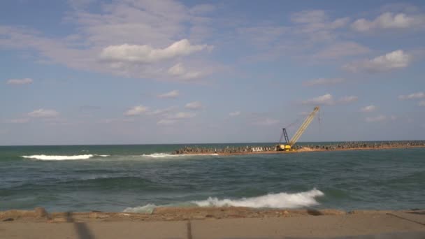 Baukran steht im Meer auf der Landenge. eine Frau geht die Promenade entlang — Stockvideo