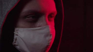 Tıbbi maskeli ve başlıklı bir adam kameraya bakıyor.