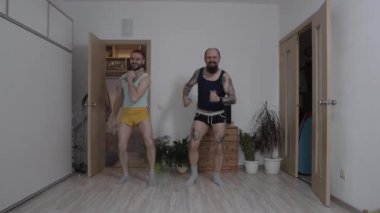 Kadın kıyafetleri içindeki erkekler evde spor yapıyor.