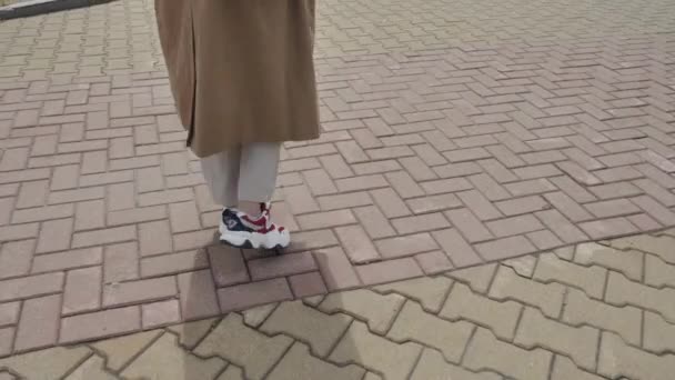 Een meisje in een loopgraaf en sneakers loopt op de stoep — Stockvideo