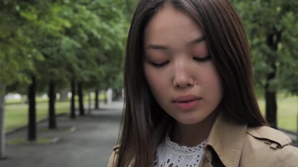 Menina atraente pensivamente fica no parque contra o fundo das árvores Filmagem De Stock