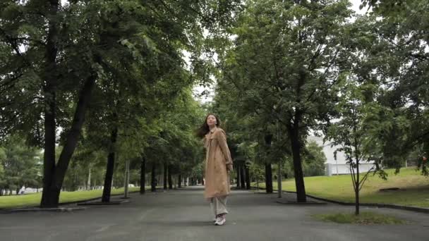 Una ragazza in un mantello marrone si trova in un parco e posa per la fotocamera — Video Stock