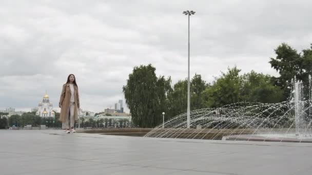 スニーカーの魅力的な女の子は噴水に沿って歩く — ストック動画