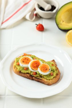 Toasted Sourdough Bread with Mashed Avocado and Sliced Boiled Egg for a Healthy Breakfast. Avocado Toast with Hard Boiled Eggs on a White Plate and Background.