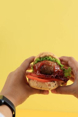 Hamburg bifteği, marul ve domatesli Kadın El Tutma Mini Burger, Sarı Arkaplanda Metin için Kopya Boşluğu ile izole edilmiş 