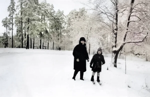 Mutlu anne ve oğulun klasik portresi. Anne oğluna kayak yapmayı öğretiyor. Karlı kış. Retro fotoğraf 1971. SSCB.