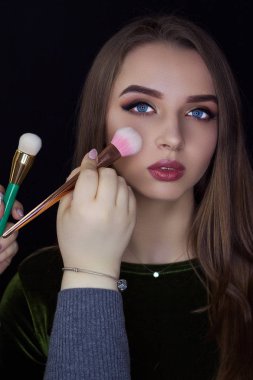 Bir kız bir siyah arka plan üzerine bir makyaj fırça tutar. Profesyonel makyaj. Biz makyaj yapmak.