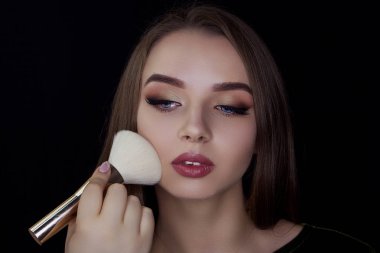 Bir kız bir siyah arka plan üzerine bir makyaj fırça tutar. Profesyonel makyaj. Biz makyaj yapmak.