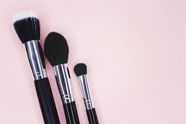 Mixed pink and tan colored glow face pearls blush, brush and puff on pink background. Top view point.