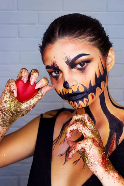 Halloween diablo hipster con cuernos y cara de maquillaje de cráneo de chica. El hombre y la mujer hacen manos de corazón. Pareja enamorada sobre fondo rojo. San Valentín, días festivos, cosplay, celebración, espacio para copiar — Foto de Stock