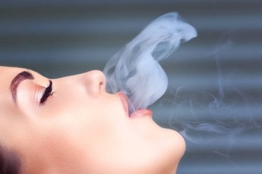 Sigara dumanı üfleyen bir kızın yüzü.