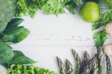 Beyaz ahşap arka plan metin için yer ile çeşitli yeşil sebze. Çerçevelemek--dan taze sebzeler: ıspanak, marul, salatalık, zencefil, limon, kuşkonmaz ve brokoli. Düz yatıyordu. Uzay kopyalayın. Üstten görünüm.