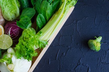 Çeşitli yeşil ve mor taze sebze, yeşillik ve meyve içinde siyah arka plan üzerine ahşap tepsi. Detoks, temiz yemek, Vejeteryan, Vejeteryan, sağlıklı yaşam konsepti. Düz yatıyordu. Üstten görünüm. Kopya alanı.