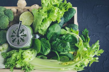 Malzemeler bir mason kavanoza sağlıklı yeşil sebze suyu: ıspanak, kereviz, salatalık, marul, zencefil, rezene, kireç ve brokoli siyah arka plan üzerine bir tepsi. Bahar Detoks kavramı. Üstten Görünüm.