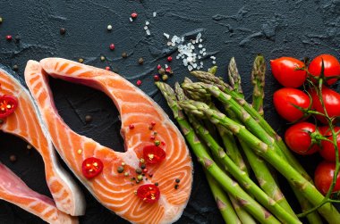 İki taze çiğ somon biftek sebze ve baharatlar ile: kuşkonmaz, domates, biber Mısır, tuz, biber biber, limon ve zeytin yağı siyah arka plan üzerine. Sağlıklı gıda diyet kavramı. Üstten görünüm.