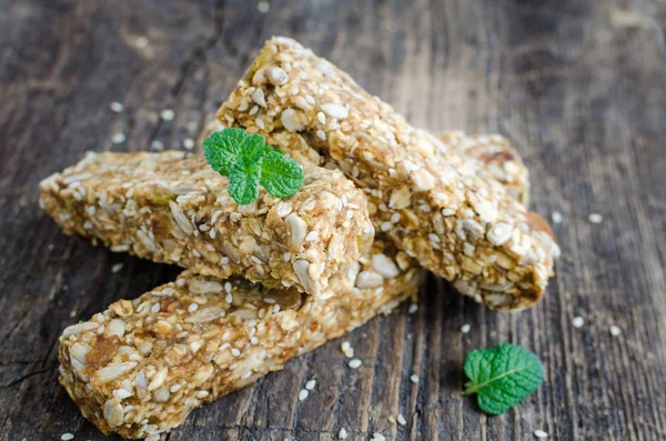 Healthy dessert snacks. Fitness dietary food. Three granola bars with oat flakes, sesame, sunflower and pumpkin seeds, raisins, honey at old rustic wooden board with mint. Vegan nutrition concept.