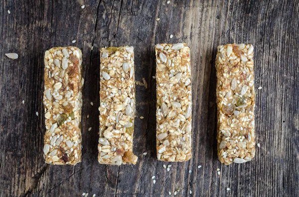 Healthy sweet dessert snacks. Fitness dietary super food. Four original energy bars with homemade granola, sesame seeds, raisins on old rustic wooden board. Vegetarian nutrition concept. Top view.