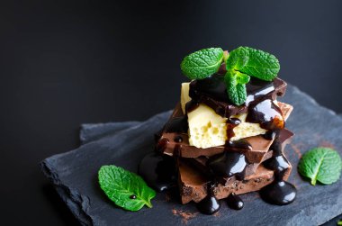 Çikolata koyu slate tahta üzerinde yeşil nane yaprakları ile eritilmiş çikolata ile siyah arka plan üzerine döktü kule yığını. Seçici odak, yakın. Kopya alanı.