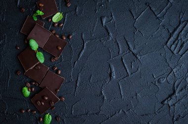 Koyu çikolata kahve çekirdekleri ve yeşil nane ile siyah arka plan üzerine bırakır. Üstten Görünüm. Kopya alanı.