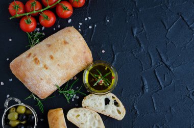 Geleneksel İtalyan ekmeği ciabatta taze pişmiş ekmek domates, biberiye, tuz, zeytinyağı ve zeytin ile siyah taş tabloda dilimlenmiş. İtalyan gıda kavramı. Üstten Görünüm. Kopya alanı.