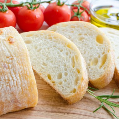 Biberiye, tuz, domates ve zeytinyağı ile beyaz rustik tabloda ahşap kesme tahtası üzerinde taze pişmiş ciabatta ekmeği dilimlenmiş. İtalyan gıda kavramı.