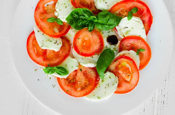 Tabak sağlıklı klasik lezzetli caprese salatası ile olgun domates ve mozzarella peyniri taze fesleğen ile beyaz ahşap zemin üzerine bırakır. İtalyan yemeği. Üstten Görünüm.