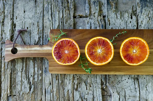 Kan portakal kekik ile ahşap tahta üzerinde dilimlenmiş. Narenciye arka plan. Olgun sulu Sicilya kan portakal meyveler üzerinde eski ahşap dokulu arka plan kes. Üstten görünüm. Kopya alanı.