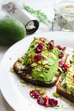 Kahvaltı veya çavdar ekmeği, krem peynir, roka, ile öğle yemeği için sağlıklı avokado tost dilimlenmiş avokado, kurutulmuş kızılcık, kabak, kenevir, susam, tuz ve biber. Vejetaryen sandviç. Temiz yemek.