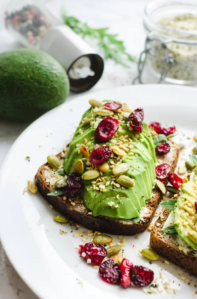 Kahvaltı veya çavdar ekmeği, krem peynir, roka, ile öğle yemeği için sağlıklı avokado tost dilimlenmiş avokado, kurutulmuş kızılcık, kabak, kenevir, susam, tuz ve biber. Vejetaryen sandviç. Temiz yemek.