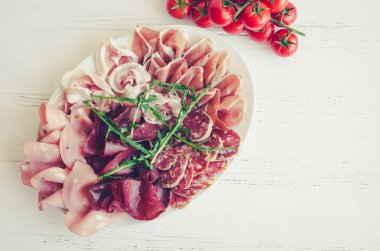 Soğuk et tabağı domuz eti, jambon, salam, bresaola, roka ve domates Beyaz ahşap arka plan üzerinde kiraz ile füme. Şarap meze küme. İtalyan yemeği. Üstten Görünüm. Kopya alanı.
