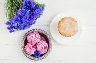 Pembe zephyr marshmallow cappuccino kahve ve Beyaz ahşap masa üzerinde mavi Peygamber buket ile. Üstten Görünüm.