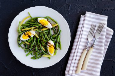 Taze yaz sıcak haşlanmış yumurta ve sos Balzamico glassa siyah taş zemin üzerine beyaz plaka ile pişmiş yeşil fasulye salatası. Sağlıklı beslenme. Vejetaryen yiyecekler kavramı. Üstten Görünüm.