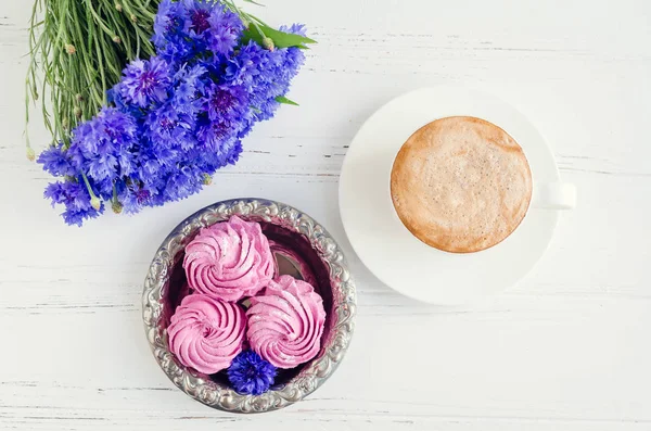 Pembe zephyr marshmallow cappuccino kahve ve Beyaz ahşap masa üzerinde mavi Peygamber buket ile. Üstten Görünüm.