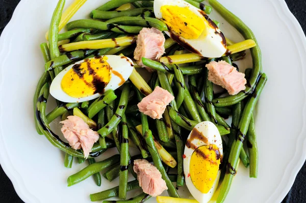 Pişmiş fasulye, ton balığı, haşlanmış yumurta ve sos Balzamico glassa siyah taş zemin üzerine beyaz tabak içinde taze yaz sıcak salatası. Sağlıklı beslenme kavramı. Üstten Görünüm.