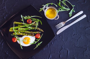 Sahanda yumurta ve domates kiraz ve roka metin için yer taş zemin üzerine siyah plaka ile kavrulmuş taze kuşkonmaz. Sağlıklı öğle yemeği kavramı. Lezzetli besleyici yemek. Üstten görünüm. Kopya alanı.