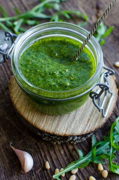 Ev yapımı roka pesto çam fıstığı, taze roka ve sarımsak eski rustik ahşap masa üzerinde bir cam kavanoza. Geleneksel İtalyan fesleğen pesto Cenevizli sos çesidi. Lezzetli sağlıklı gıda.