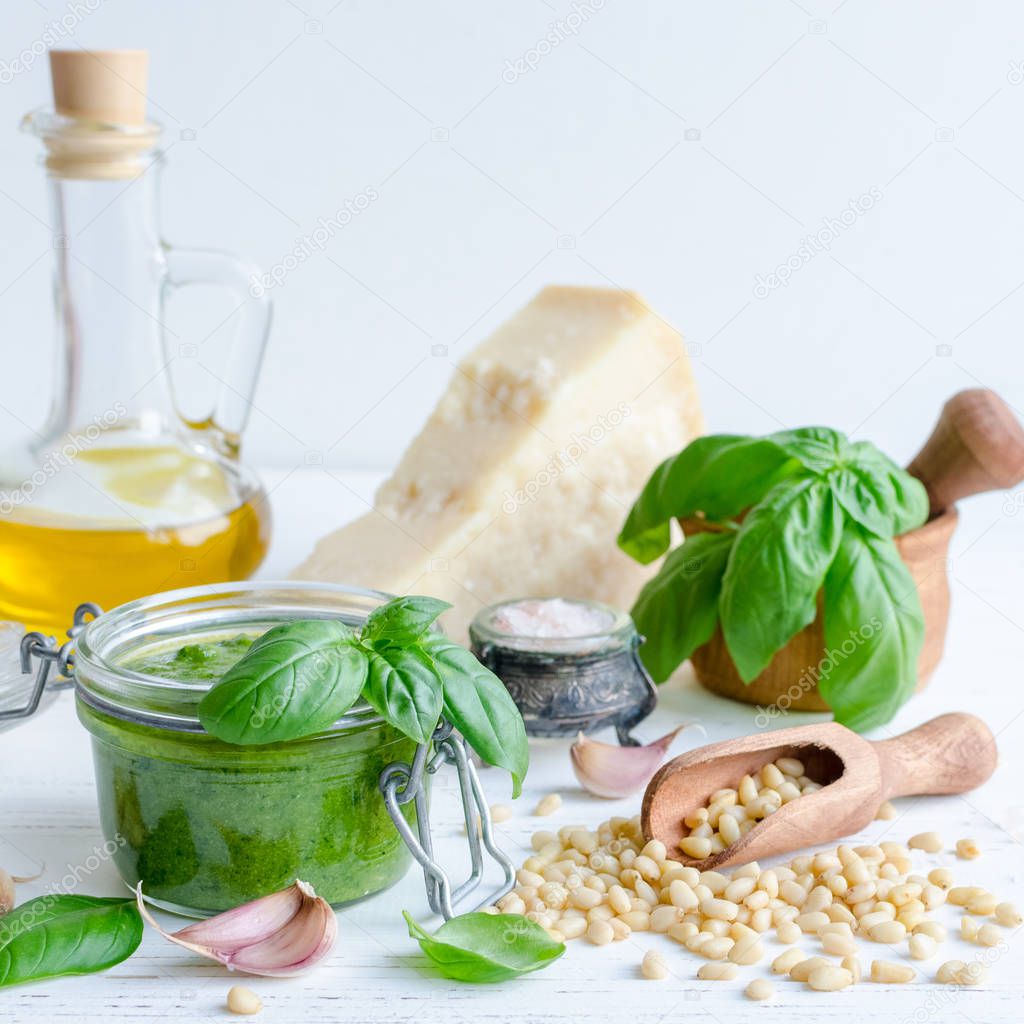 Pesto genovese - traditional Italian green basil sauce with raw ingredients on white wooden background. Basil leaves in mortar, Parmesan cheese, pine nuts, olive oil, garlic and salt.