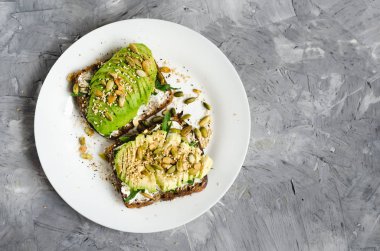 Kahvaltı veya çavdar ekmeği, avokado, roka, kabak ve susam, tuz ve biber dilimlenmiş ile öğle yemeği için sağlıklı avokado kızartır. Vejetaryen yiyecekler. Bitki temelli diyet. Temiz yemek. Üstten görünüm. Kopya alanı.