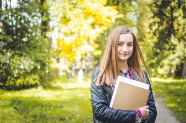 Öğrenci kız açık havada Park okula dönecek ve gülümseyerek. Genç ya da genç yetişkin yüksek okul veya üniversite öğrencisi kameraya bakıyor. Kız bir sırt çantası giyiyor ve ders kitapları holding.