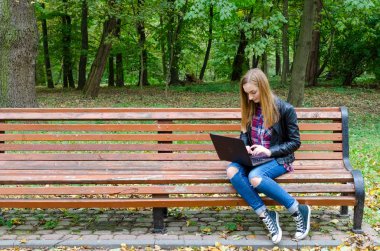 Açık havada okuyan öğrenci. Genç kadın parkta bankta otururken dizüstü bilgisayarda klavye. Sarışın kadın teen sonra onun ders Üniversitesi'nde net-kitap üzerinde çalışıyor. Metin için yer kopyalayın.